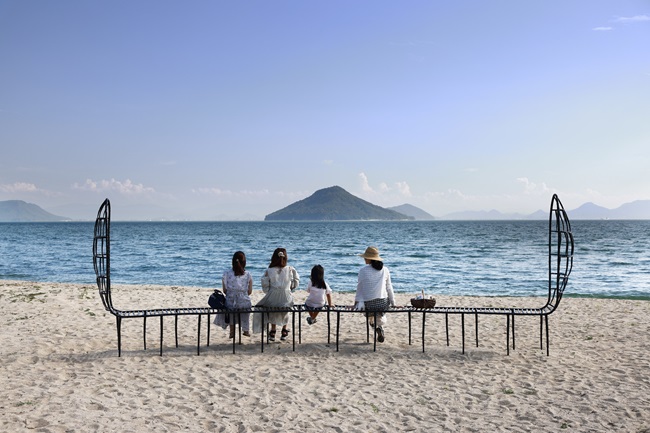 Drei Frauen und ein Mädchen sitzen auf der Gitternetzbank am Strand der Insel Teshima und blicken aufs Meer