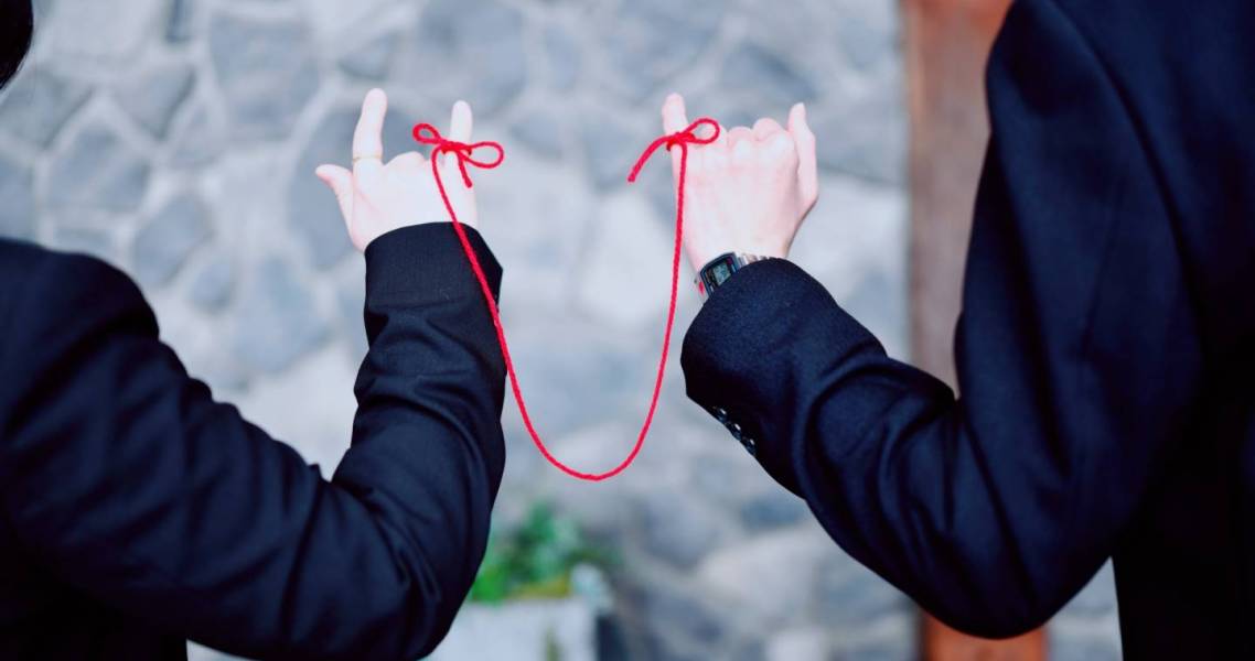 Zwei Menschen sind mit einem roten Faden um ihre kleinen Finger miteinander verbunden