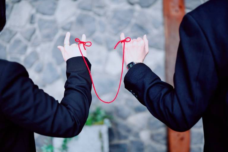 Zwei Menschen sind mit einem roten Faden um ihre kleinen Finger miteinander verbunden